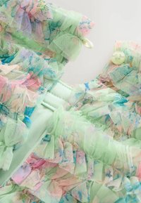 Pasztellzöld szövet áttetsző tüll fodrokkal, pasztell rózsaszín és kék akvarell mintákkal; világoszöld gombokkal rögzítve.