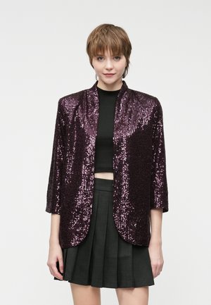 Veste en sequins de couleur violet profond avec une coupe décontractée, col châle et manches trois-quarts, présentant une texture lisse et une surface chatoyante.