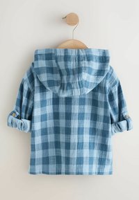 Blå ternet skjorte med hætte, fremstillet i et tekstureret stof med op-rullede ærmer, som er fastgjort med knapper, hængende på en træbøjle.