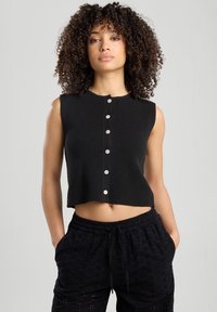 Musta lyhythihainen toppi, jossa on ribbikuviointi ja pyöreä kaula-aukko, etupuolella hopeanväriset napit.