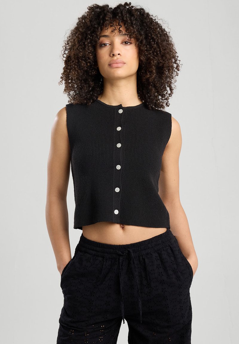 Musta lyhythihainen toppi, jossa on ribbikuviointi ja pyöreä kaula-aukko, etupuolella hopeanväriset napit.