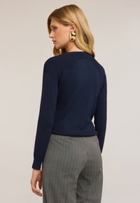 Námořnický vzorovaný pletený svetr s dlouhými rukávy, s přiléhavým siluetou. V kombinaci se šedými kalhotami s proužky.