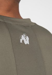 Olijfgroene sportshirt met een gestructureerde afwerking, met een wit gorilla-logo op de achterkant. Klassiek ronde hals ontwerp.