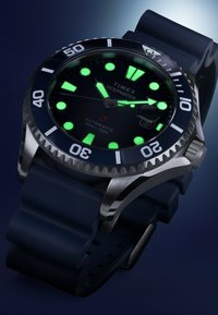 Zegarek Timex Deepwater z czarną tarczą, świecącymi znacznikami, stalową ramką i niebieskim gumowym paskiem, z oceną odporności na wodę do 200 m.