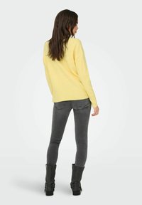 Žuti rebrasti pulover s opuštenim krojem, uparen s uskim sivim trapericama i crnim čizmama do koljena s detaljima kopčanja.