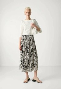 Witte top met lange mouwen gecombineerd met een zwarte midi-rok met ingewikkelde witte bloemenbroderie. Kleur geblokkeerde blokhak sandalen maken de look compleet.