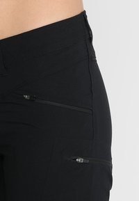 Pantalon de randonnée noir en tissu lisse et extensible. Doté de plusieurs poches zippées et d'une taille ajustée. Convient pour les activités en plein air.