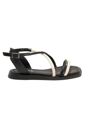 Sandales noires et blanches à talon plat, en cuir lisse, avec une bride ajustable à la cheville, présentant un design minimaliste.