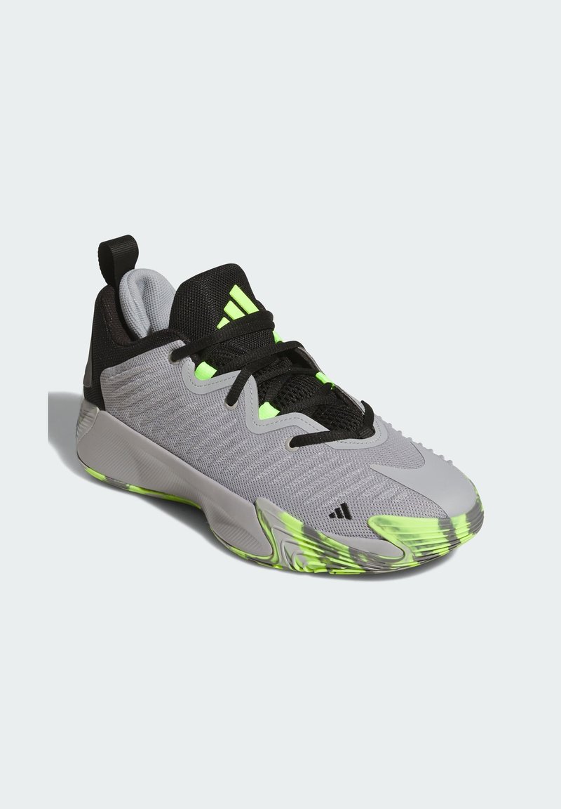 Baskets de sport grises avec accents noirs, présentant un dessus texturé, des détails en néon vert et une semelle en caoutchouc flexible avec des motifs distincts.