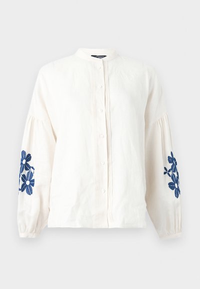 Λευκό μπλουζάκι με μακριά μανίκια, κουμπιά μπροστά, σούρα στα μανίκια και μπλε κέντημα με λουλούδια και στα δύο μανίκια.