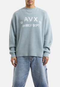 Lichtblauwe geribbelde gebreide trui met witte geborduurde tekst "AVX 19 AVREX DEPT." Ontspannen pasvorm met verlaagde schouders en wijde mouwen.