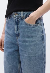 Jean en denim bleu clair avec un design classique à cinq poches, une fermeture par bouton et un léger effet délavé sur le tissu pour plus de texture.