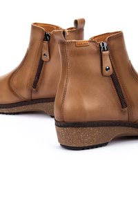 Bottines en cuir marron avec des zips latéraux, semelles texturées et un petit talon, avec une base semblable à du liège et des détails de couture contrastants.
