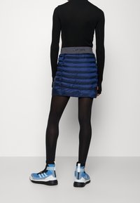 Marinblå puffkjol med horisontella sömmar, med ett grått midjeband. I kombination med blå högklackade sneakers och svarta tights.