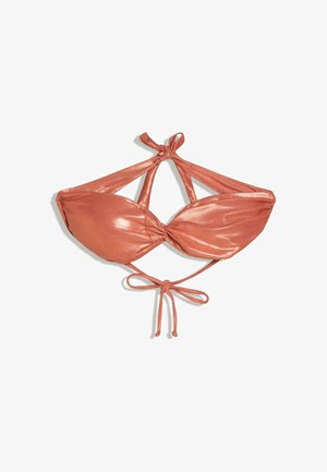 Junge Frau mit nassen Haaren, die ein glänzendes, rostfarbenes Bandeau-Bikinitop trägt, steht vor dem sonnenbeschienenen Meer und entfernten Inseln bei Sonnenuntergang.