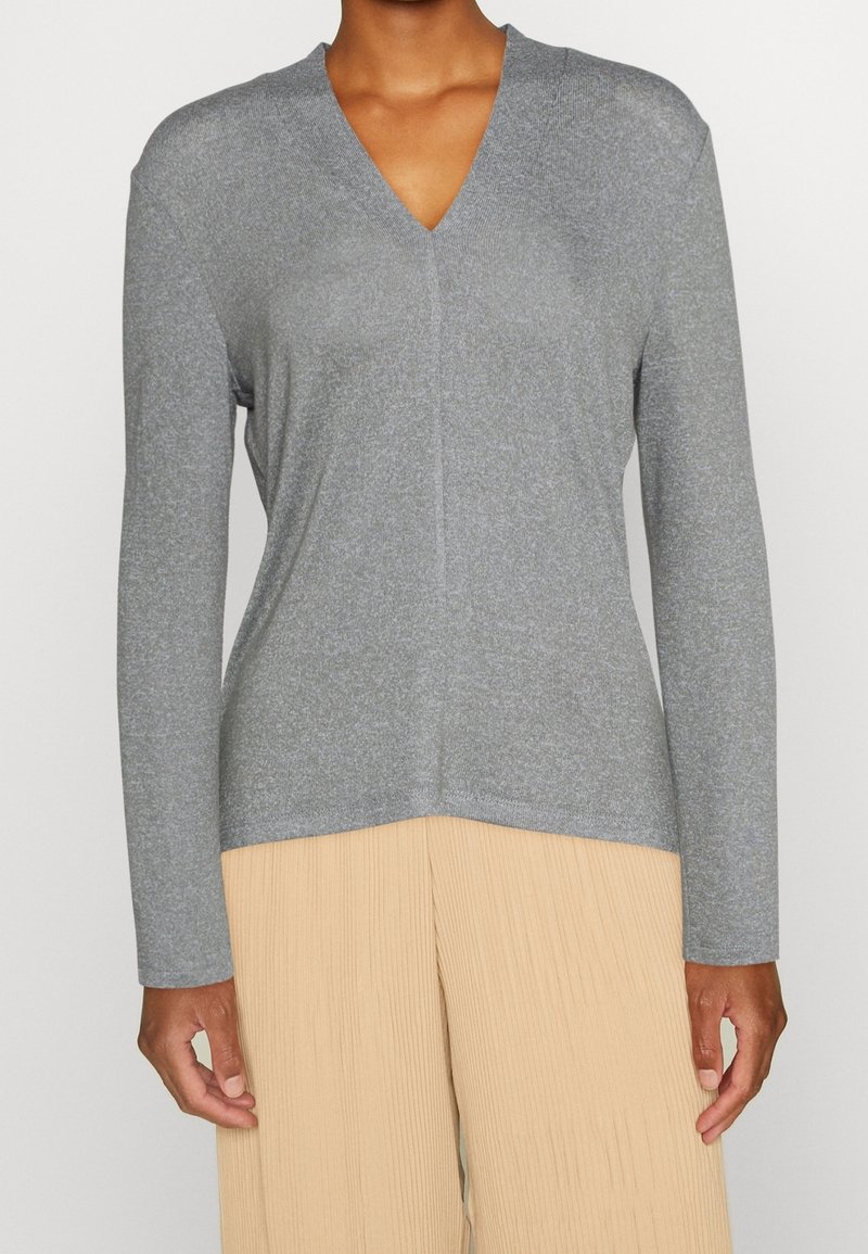 Grå långärmad V-ringad topp gjord av ett mjukt, texturerat tyg, med en enkel design och en något längre bakre fållen.