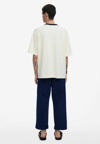 Loose-fitting cream cotton t-shirt with a dark neckline, paired with navy wide-leg trousers, featuring rolled cuffs and simple sandals.