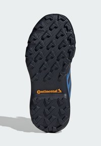 Czarna gumowa podeszwa buta z teksturowanym bieżnikiem i wyraźnym, pomarańczowym logo Continental. Po bokach widoczne niebieskie akcenty.