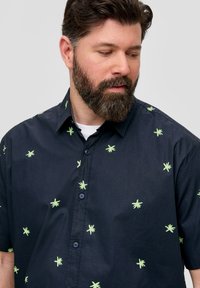 Chemise à manches courtes en tissu bleu marine, ornée de motifs de feuilles vertes éparpillées et de boutons bleus, avec un col classique.