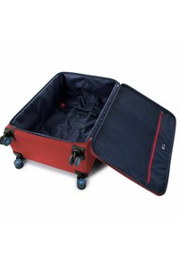 Valigia rigida rossa con interno blu navy, chiusura a zip e quattro ruote blu. L'interno include un cinturino e una tasca con zip in rete.