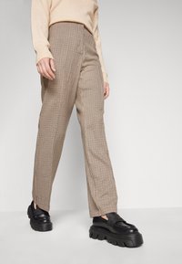 Pantalon à carreaux beige et marron, doté d'une taille haute, d'une coupe droite et d'un tissu texturé. Associé à des chaussures à plateforme noires.