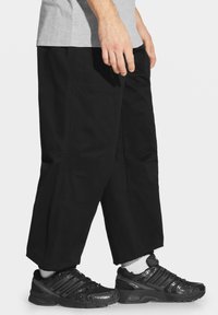 Czarne spodnie cargo wykonane z mocnego materiału z bocznymi kieszeniami, zestawione z czarnymi butami sportowymi i białymi skarpetkami, przedstawione od pasa w dół.