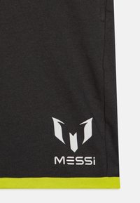 Zwarte sportieve shirt met een wit logo en de tekst "MESSi" op de linksonderkant, met een felgele rand aan de onderkant. Zachte stofstructuur.