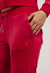 Fuchsia joggers van zachte, gestructureerde stof met zijzakken. Beschikt over een geborduurd logo op de zak en een verstelbare drawstring tailleband.
