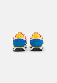 Puma-Sneaker mit einer blauen Wildlederferse, roten und gelben Akzenten, weißem Mesh und einer schwarzen Gummisohle mit strukturiertem Grip-Muster.