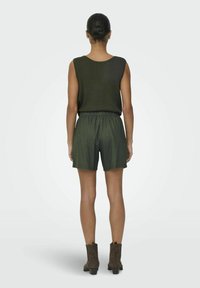 Groene geribbelde tanktop gecombineerd met bijpassende shorts; elastische tailleband; model draagt bruine enkellaarzen met decoratieve stiksels.