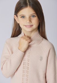 Maglione rosa chiaro in maglia con collo alto a coste, motivo strutturato al centro e piccolo logo sul petto. Materiale morbido.