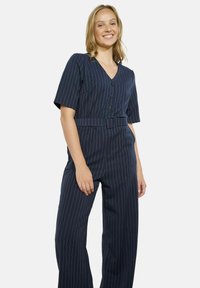 Granatowy kombinezon w pinstriped z krótkimi rękawami, z zapięciem na guziki i paskiem w talii. Tkanina ma gładką powierzchnię z pionowymi liniami.