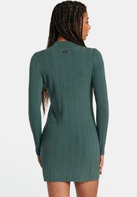 Vestido de manga larga de canalé en color azul verdoso con silueta ajustada. Presenta un escote redondo y una sutil etiqueta de la marca en la parte posterior. Textura suave.