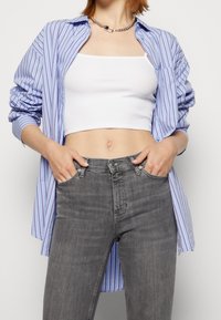 Camisa de rayas azul claro y blanca de manga larga sobre una camiseta corta blanca sencilla, combinada con unos vaqueros de tiro alto grises.
