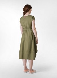 Vestido verde caqui con mangas cortas, cintura ajustada y dobladillo asimétrico. Presenta una pequeña etiqueta rosa en la parte posterior. Se lleva con zapatos de color rosa claro.