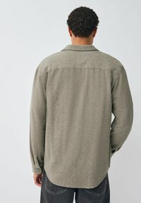 Green houndstooth-patterned shirt made of textured fabric, featuring a buttoned cuff and a straight hem, viewed from the back.