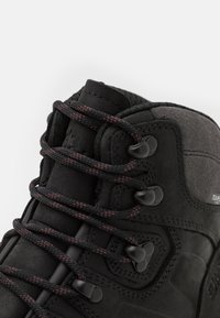 Schwarzer Wanderschuh mit textured Leder- und Wildlederschaft, ausgestattet mit schwarzen und roten Schnürsenkeln, Kunststoffösen und Nahtdetails.