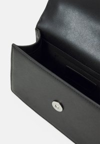 Interiér černé kožené tašky s hladkou texturou, magnetickým zavíráním a elegantním designem s přihrádky na karty.