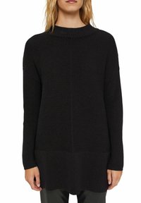 Svart stickad tröja med ribbat mönster, har hög hals, långa ärmar och en något längre bakre fåll.