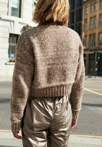 Kort, texturerad tröja i beige garn med ribbad nederkant, ihop med glänsande metalliska silverbyxor med sidofickor.