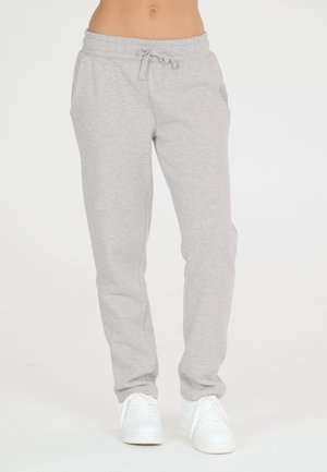 Graue Baumwoll-Sweatpants mit elastischem Bund und Kordelzug. Mit Seitentaschen und schmal zulaufenden Beinen, kombiniert mit weißen Turnschuhen.