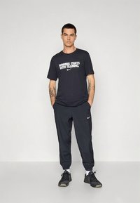 Must Nike t-särk valge tekstiga "VIIGID ALGAVAD TRENNIST", millel on mustad spordipüksid ja mustad spordijalatsid.
