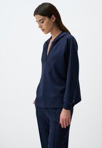 Felpa blu navy con scollatura a V profonda e maniche raglan. Realizzata in un tessuto morbido, presenta una vestibilità comoda e spacchi laterali per il massimo comfort.