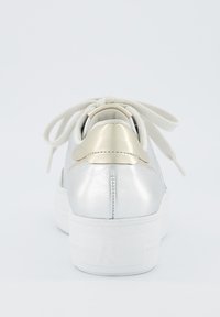 Sneaker metallica argento con suola bianca, caratterizzata da un dettaglio dorato sul tallone e lacci beige, texture liscia e forma tonda.