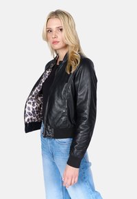 Giubbotto bomber in pelle nera con polsini e orlo a coste, con foderatura a stampa leopardata. Il modello indossa jeans azzurri.