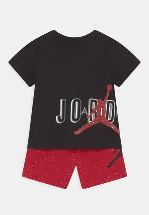 Czarna koszulka z krótkim rękawem z czerwonym napisem "JORDAN" i logo Jumpman, zestawiona z czerwonymi szortami w cętki.
