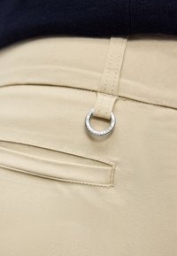 Μπεζ παντελόνι με πίσω τσέπη με λάστιχο και θηλιά για ζώνη που ασφαλίζεται με μικρό ασημένιο δαχτυλίδι με χαραγμένη την ένδειξη "DAILY SPORTS".