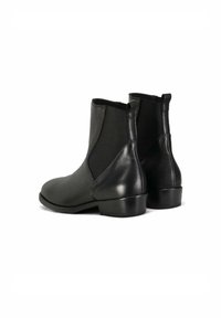 Stivali ankle in pelle nera con tacco basso e pannelli elastici laterali, visti da dietro su uno sfondo bianco.