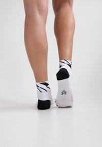 Weiße Knöchelsocken mit schwarzen Streifen und Akzenten, die ein Logo tragen und eine weiche Textur sowie ein sportliches Design aufweisen.