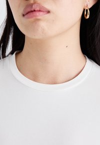 White t-shirt with a round neckline, soft texture, and smooth finish, paired with a gold hoop earring. Skin tone and details visible.
